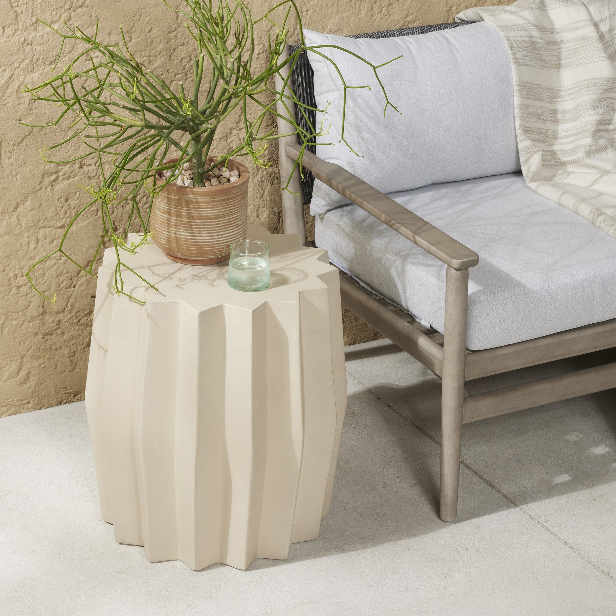 Mesa lateral para exteriores Olenna color pergamino blanco en un patio exterior.